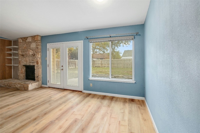 unfurnished living room with a stone fireplace, french doors, and light wood-type flooring