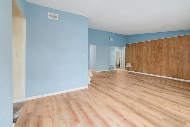 spare room featuring wood walls, vaulted ceiling, and light hardwood / wood-style flooring