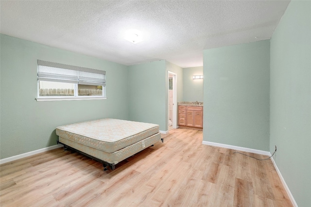 bedroom featuring light hardwood / wood-style floors, a textured ceiling, and connected bathroom