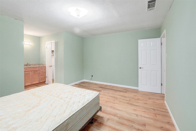 bedroom featuring connected bathroom, sink, a textured ceiling, and light wood-type flooring