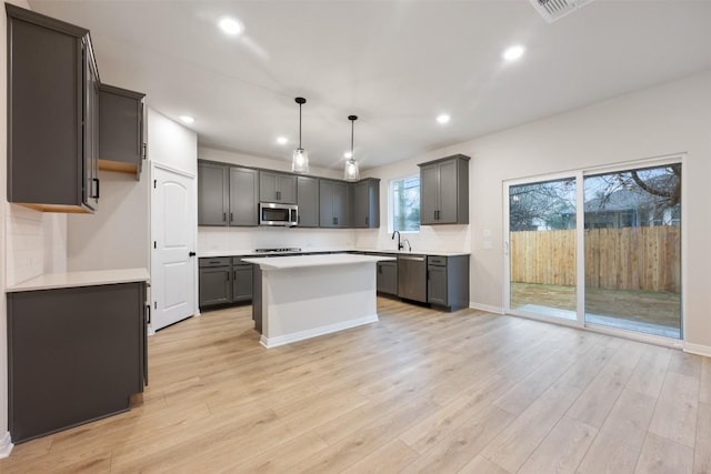 kitchen featuring light hardwood / wood-style flooring, a kitchen island, gray cabinetry, decorative light fixtures, and stainless steel appliances