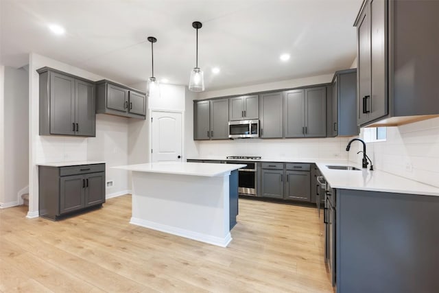 kitchen with appliances with stainless steel finishes, light hardwood / wood-style flooring, gray cabinets, a kitchen island, and sink