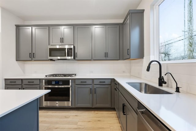 kitchen with appliances with stainless steel finishes, sink, light hardwood / wood-style flooring, gray cabinetry, and decorative backsplash