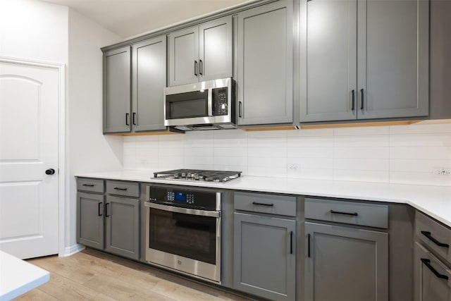 kitchen featuring appliances with stainless steel finishes, gray cabinets, tasteful backsplash, and light wood-type flooring