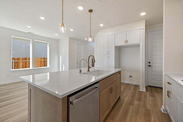 kitchen featuring a center island with sink, sink, hanging light fixtures, stainless steel dishwasher, and white cabinetry