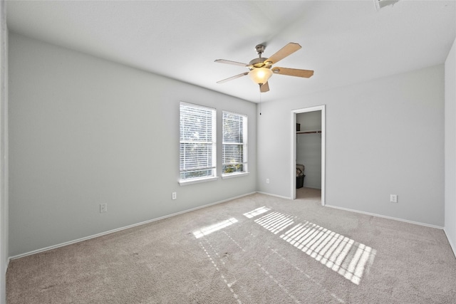 unfurnished bedroom with light carpet, a walk in closet, a closet, and ceiling fan