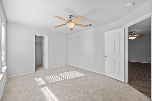 unfurnished bedroom with a walk in closet, a closet, ceiling fan, and light colored carpet