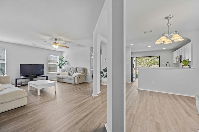 living room with ceiling fan with notable chandelier and light hardwood / wood-style flooring