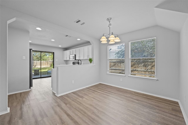 unfurnished dining area featuring light hardwood / wood-style floors, an inviting chandelier, lofted ceiling, and sink