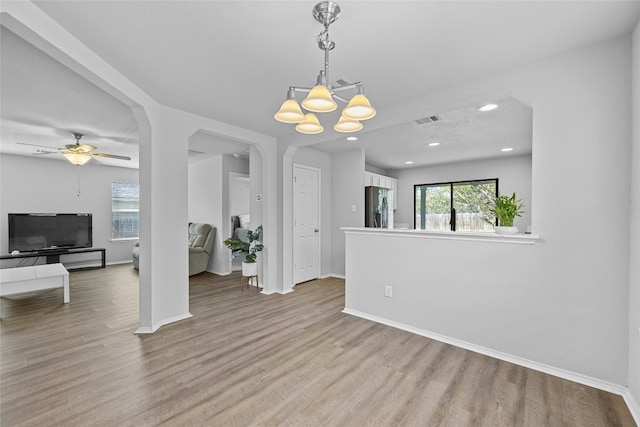 unfurnished dining area with ceiling fan with notable chandelier and light hardwood / wood-style flooring