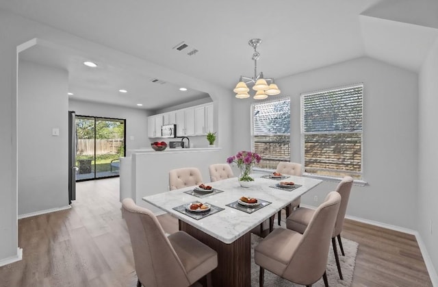 dining area with lofted ceiling, a notable chandelier, and light wood-type flooring