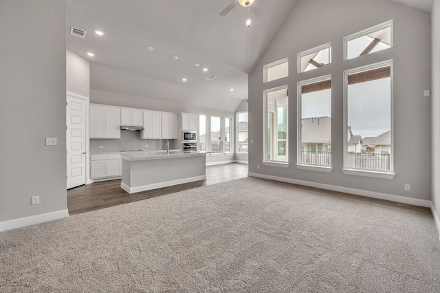 kitchen with open floor plan, a kitchen island with sink, light countertops, dark colored carpet, and white cabinetry