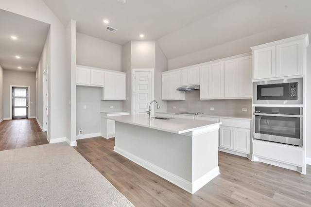 kitchen with visible vents, oven, a kitchen island with sink, built in microwave, and white cabinetry