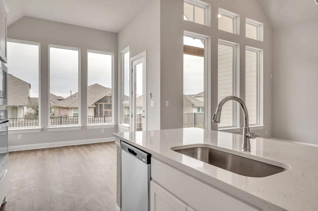 kitchen with light stone counters, vaulted ceiling, a sink, and stainless steel dishwasher