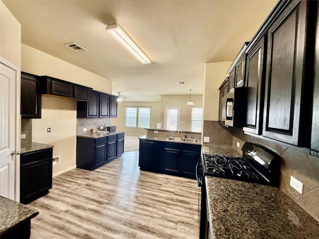 100 Wilson Ct, Hutto, TX 78634 - kitchen featuring light wood finished floors, a peninsula, ceiling fan, backsplash, and dark stone countertops