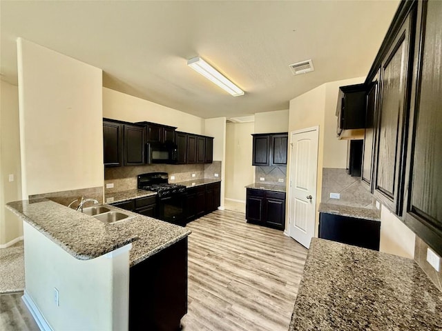 100 Wilson Ct, Hutto, TX 78634 - kitchen featuring black appliances, a peninsula, light stone countertops, decorative backsplash, and light wood-type flooring