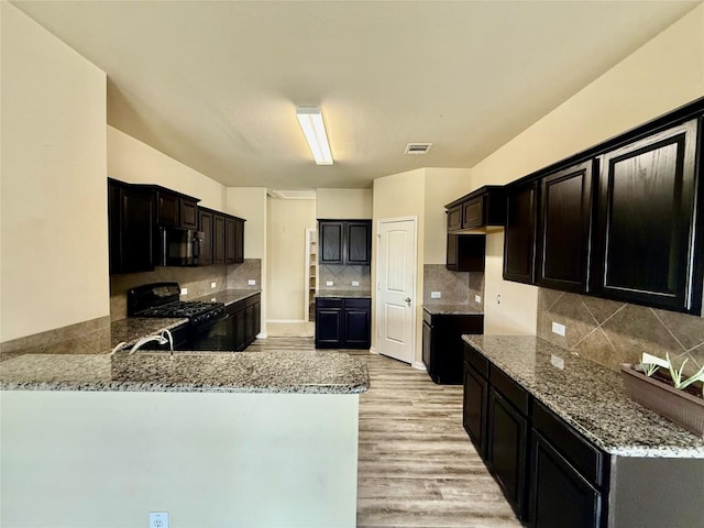 100 Wilson Ct, Hutto, TX 78634 - kitchen featuring black range with gas stovetop, light stone countertops, a peninsula, light wood-style floors, and backsplash