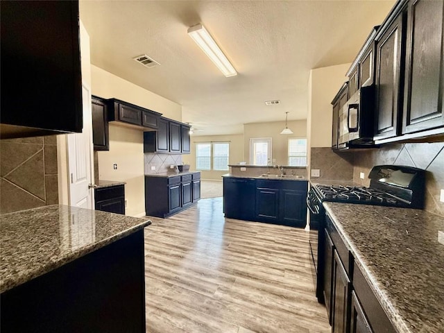 kitchen featuring black gas range oven, hanging light fixtures, decorative backsplash, dark stone counters, and light wood-type flooring