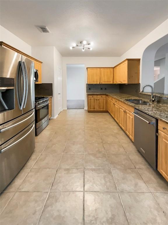 kitchen with dark stone countertops, sink, stainless steel appliances, and light tile patterned flooring