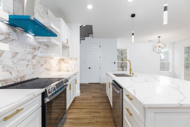 kitchen featuring appliances with stainless steel finishes, wall chimney exhaust hood, sink, pendant lighting, and an island with sink