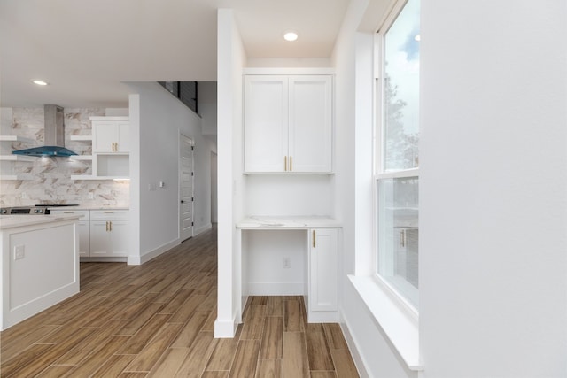 kitchen with white cabinets, decorative backsplash, light hardwood / wood-style flooring, and wall chimney range hood