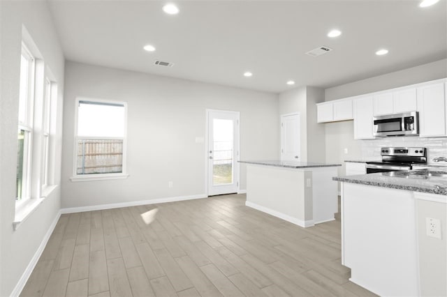 kitchen featuring white cabinets, a healthy amount of sunlight, stainless steel appliances, and dark stone counters