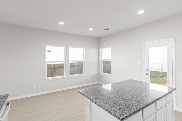 kitchen with a wealth of natural light, white cabinets, light wood-type flooring, and a kitchen island