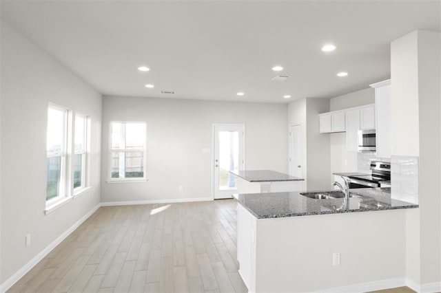 kitchen featuring light wood-type flooring, dark stone counters, stainless steel appliances, sink, and white cabinets