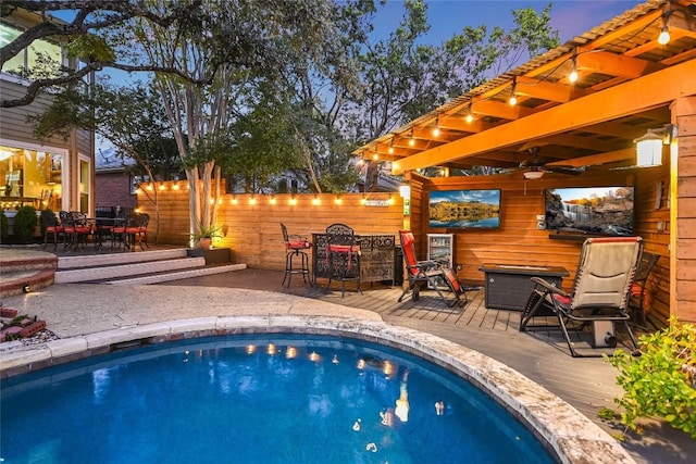 pool at dusk with ceiling fan and a deck