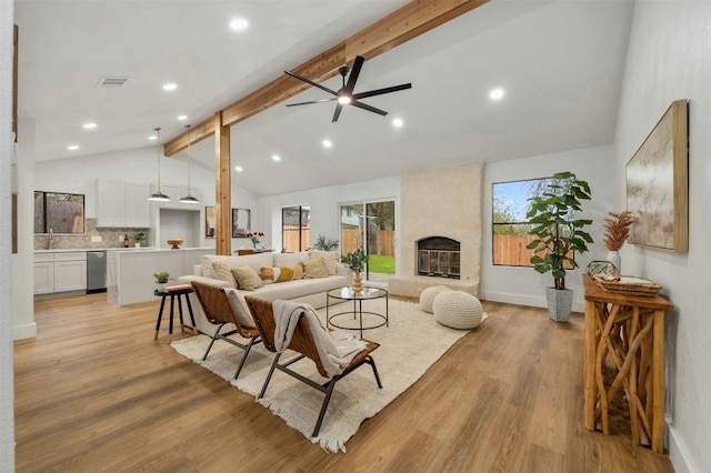 living room featuring ceiling fan, a fireplace, beam ceiling, and light wood-type flooring