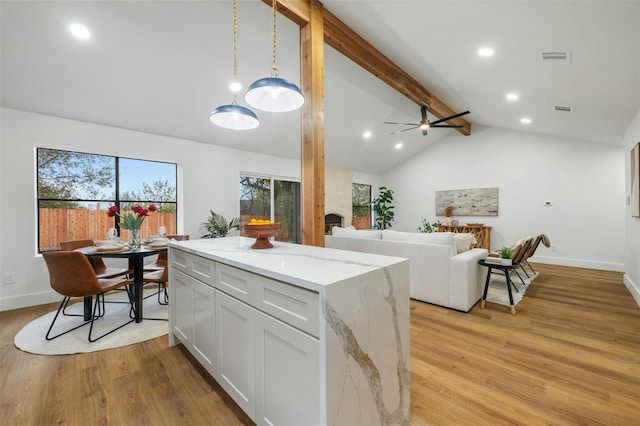 kitchen with light stone counters, light hardwood / wood-style flooring, lofted ceiling with beams, and white cabinets