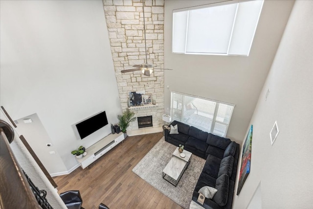 living room with ceiling fan, a fireplace, dark wood-type flooring, and a high ceiling