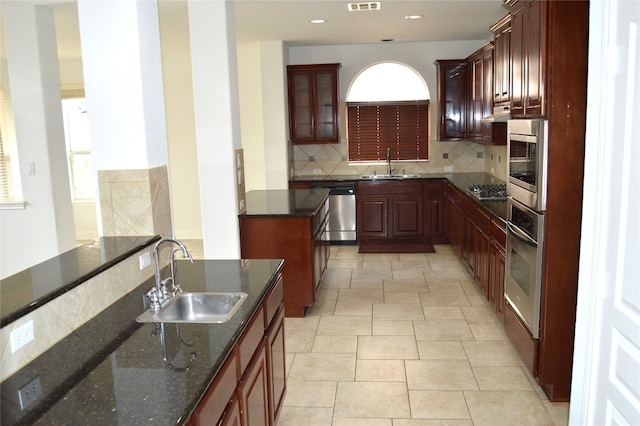 kitchen featuring backsplash, sink, dark stone counters, and stainless steel appliances