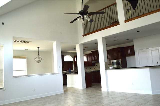 interior space featuring stainless steel microwave, decorative backsplash, ceiling fan, a towering ceiling, and dark brown cabinets