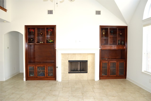 unfurnished living room with high vaulted ceiling, ceiling fan, a wealth of natural light, and a tiled fireplace