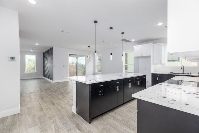 kitchen featuring a healthy amount of sunlight, pendant lighting, light hardwood / wood-style flooring, white cabinetry, and a large island