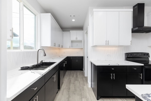 kitchen featuring sink, black appliances, wall chimney range hood, light hardwood / wood-style floors, and white cabinetry