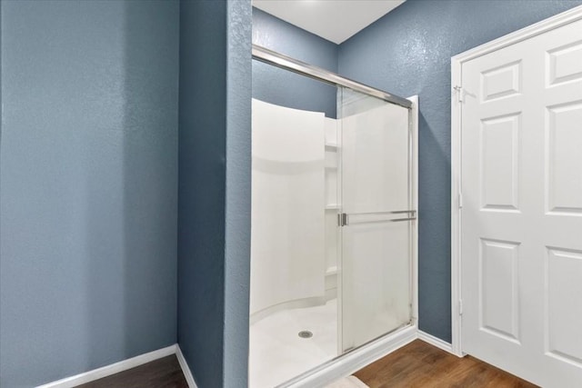 full bath featuring a textured wall, a shower stall, baseboards, and wood finished floors