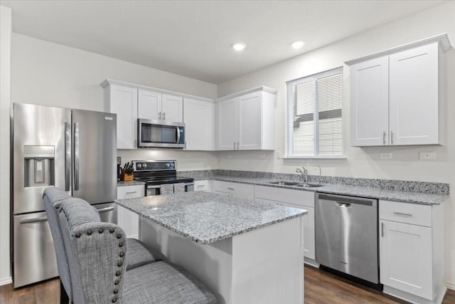 kitchen with sink, white cabinetry, appliances with stainless steel finishes, a kitchen island, and light stone countertops