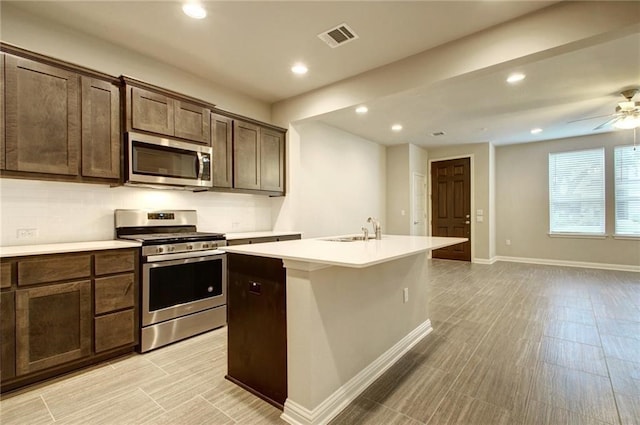 kitchen with a kitchen island with sink, sink, ceiling fan, dark brown cabinetry, and stainless steel appliances