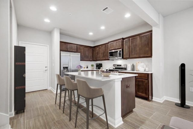 kitchen with a kitchen breakfast bar, dark brown cabinetry, stainless steel appliances, a kitchen island with sink, and sink