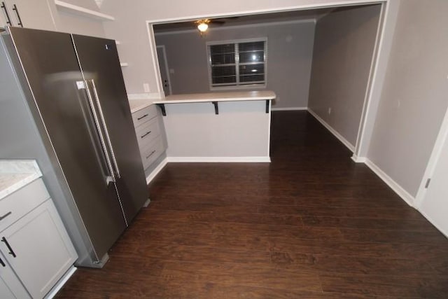 kitchen with white cabinets, kitchen peninsula, dark wood-type flooring, and stainless steel refrigerator