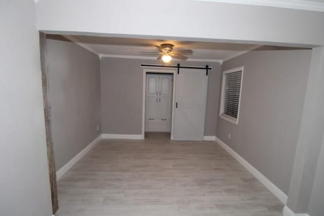 empty room with a barn door, ceiling fan, light hardwood / wood-style floors, and ornamental molding