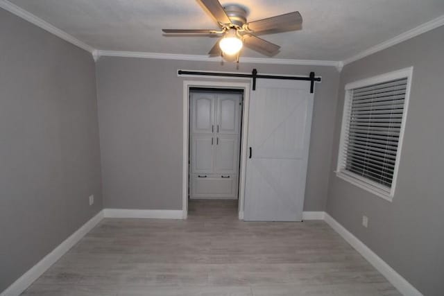 unfurnished bedroom with a barn door, light hardwood / wood-style flooring, ceiling fan, and ornamental molding