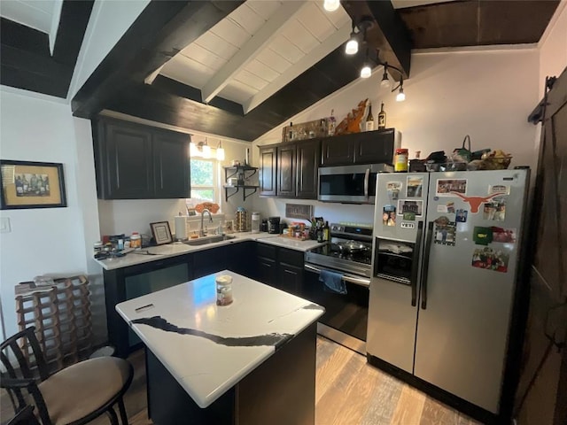 kitchen with a center island, sink, vaulted ceiling with beams, appliances with stainless steel finishes, and light hardwood / wood-style floors