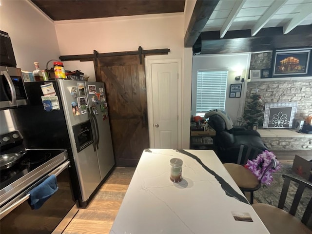 kitchen with a barn door, a stone fireplace, light wood-type flooring, and appliances with stainless steel finishes