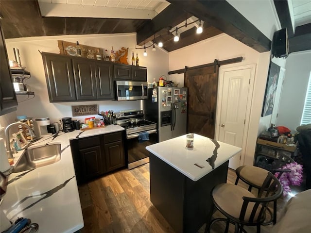 kitchen featuring sink, light hardwood / wood-style flooring, vaulted ceiling with beams, a barn door, and appliances with stainless steel finishes