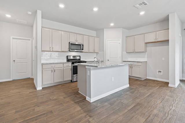 kitchen with a center island with sink, light stone counters, dark wood-type flooring, and appliances with stainless steel finishes