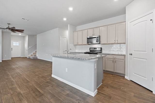 kitchen featuring light stone countertops, appliances with stainless steel finishes, a center island with sink, and dark hardwood / wood-style floors