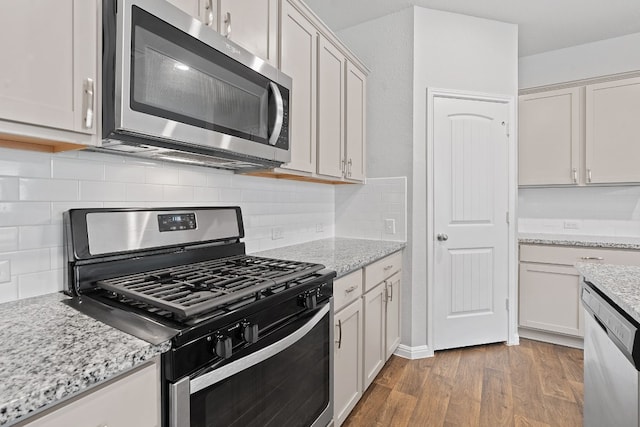 kitchen featuring backsplash, hardwood / wood-style flooring, light stone countertops, and appliances with stainless steel finishes